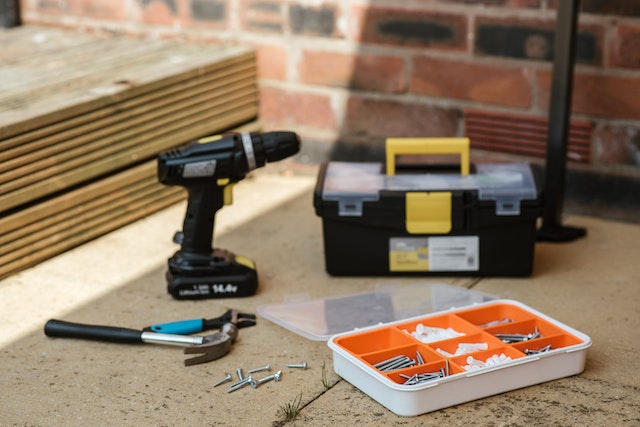 a drill, black tool box and a orange kit full of nails and screws
